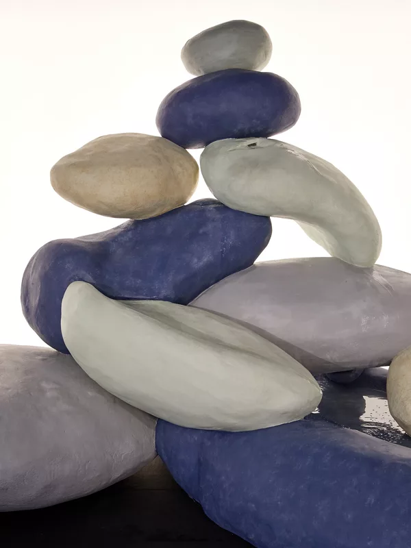 A sculpture of large violet, green, gray, and off-white stone-like objects arranged in a pile, approximately 10 objects and the sculpture is roughly 8 feet tall.