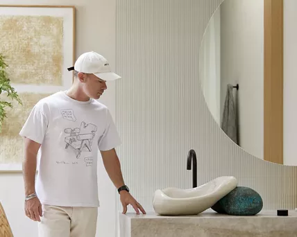 Daniel Arsham standing in a bathroom with his hand on the countertop as he looks down at the Rock.01 sink.